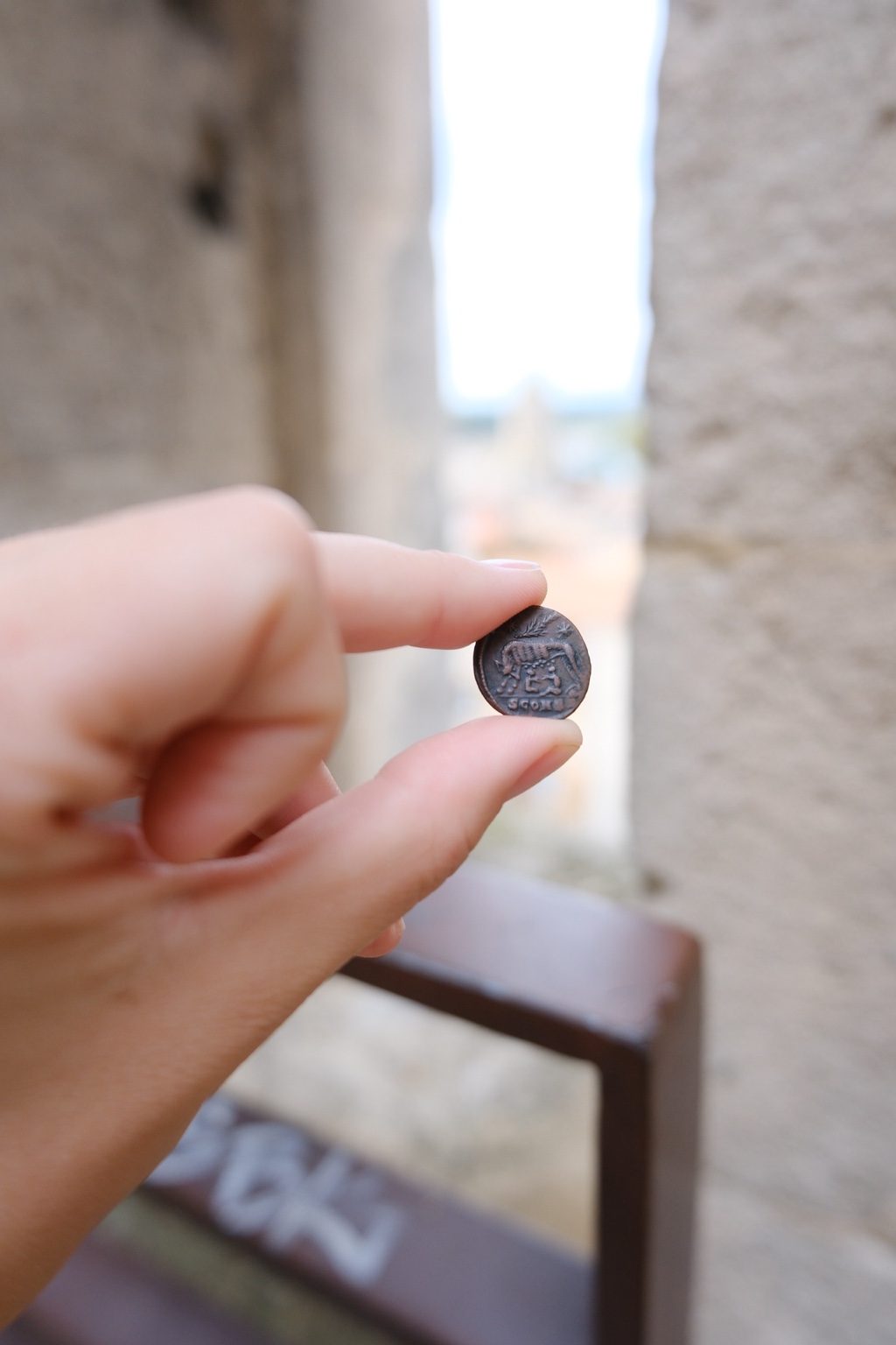 The wolf-and-twins side of the coin held between the stone walls of the Arles amphitheatre.